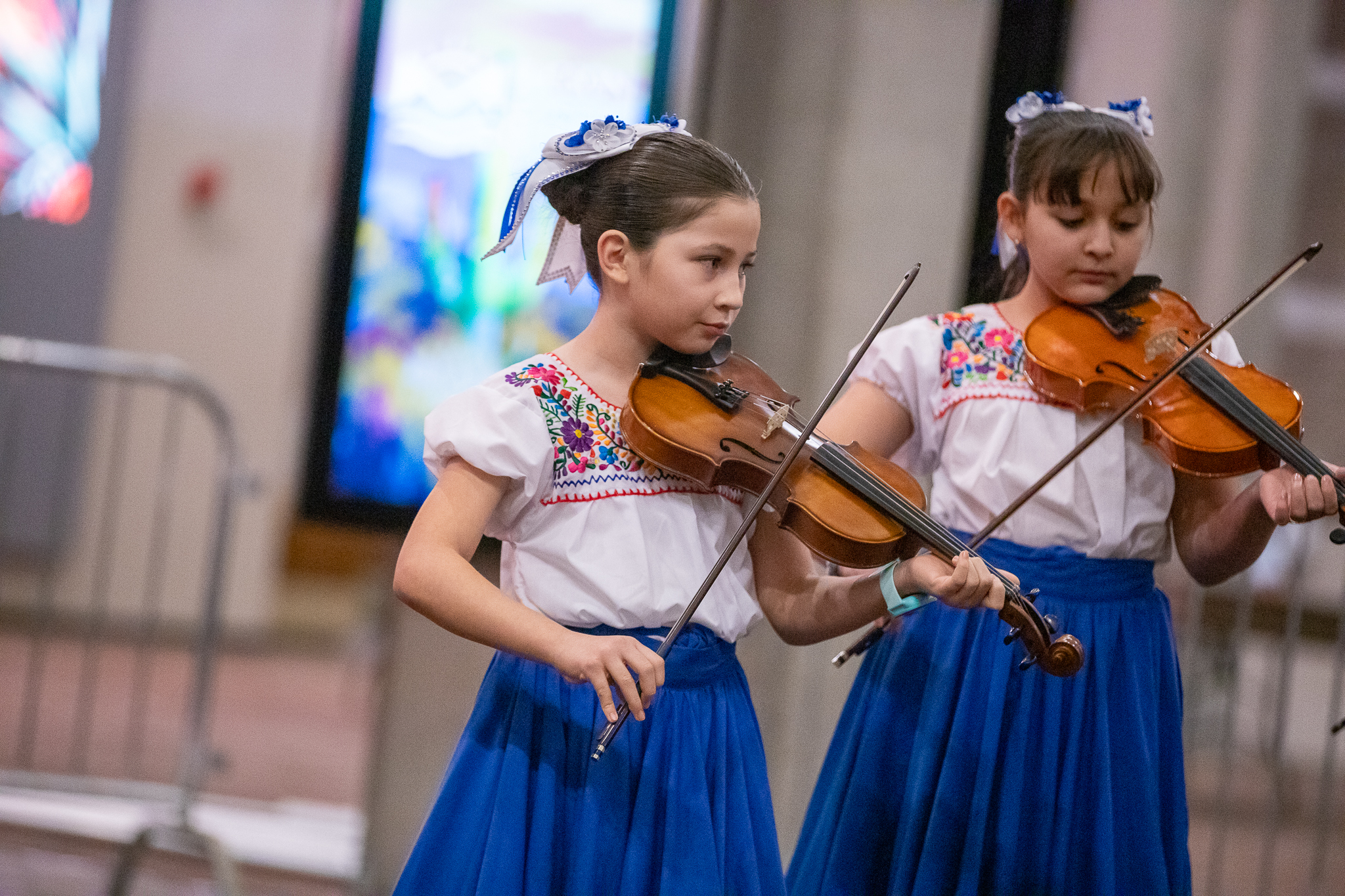 Two girls in blue and white folklorico dresses play violin