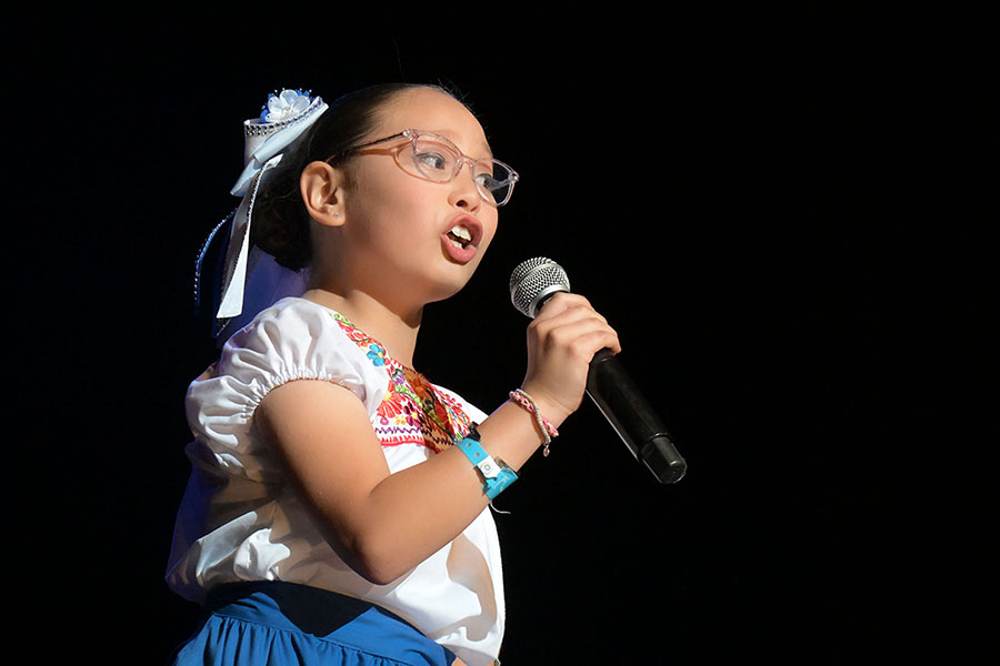 A girl with glasses sings into a mic