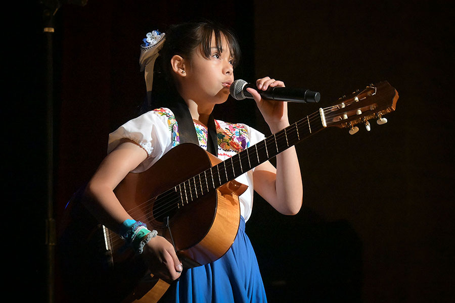A girl holding a guitar sings into the mic