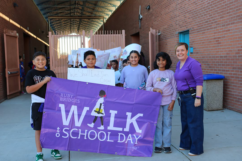 Students smile holding a purple Ruby Bridges Walk to School Day banner