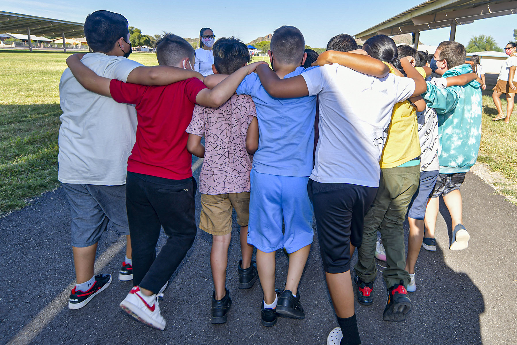 A group of boys huddle together with their backs towards the camera out at recess